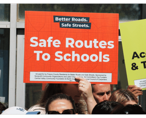 Advocate of Better Roads Safe Streets holds up a sign "Safe Routes To Schools" outside of the Fresno County Elections Office during press event announcing the submission of over 32,000 signatures to advance transportation measure toward November ballot